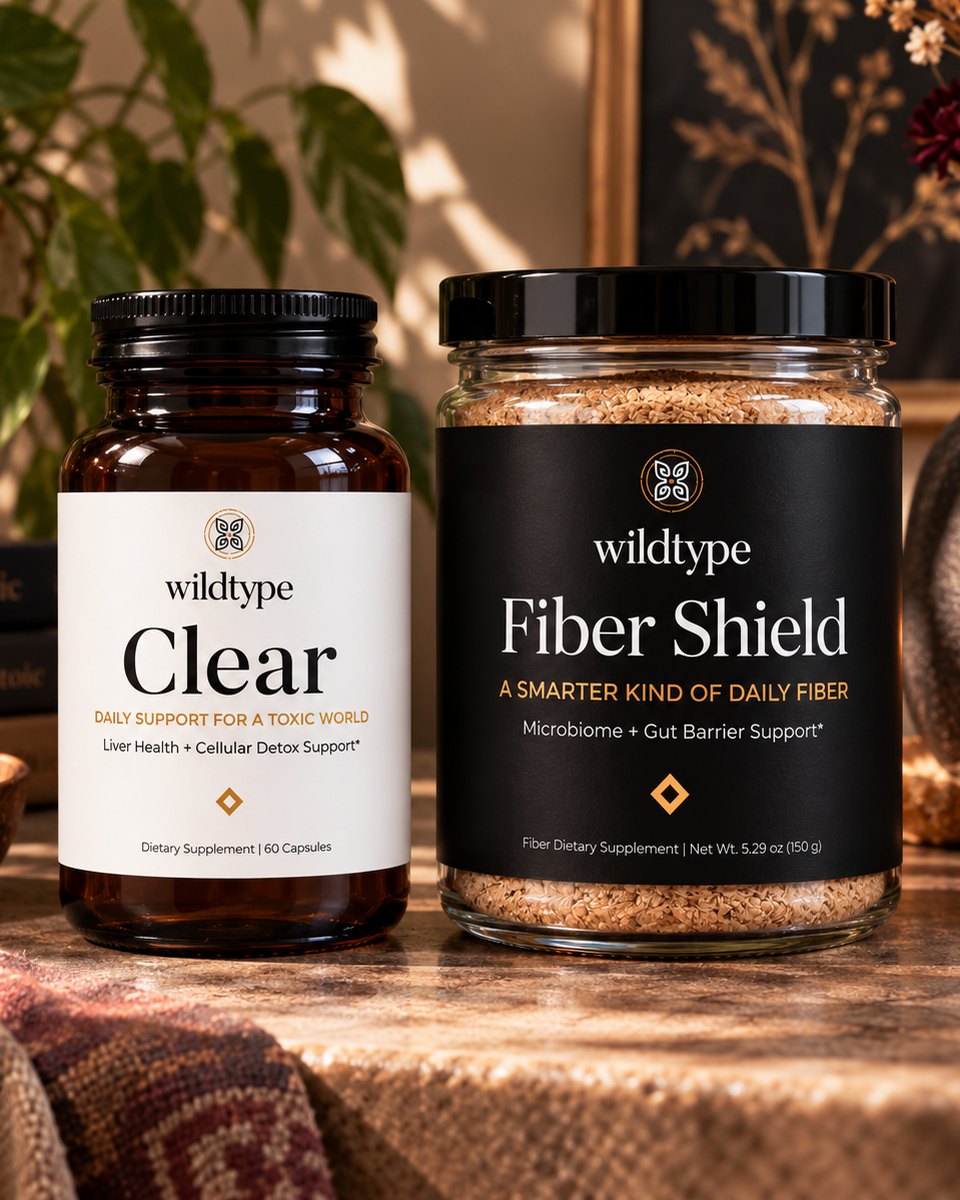 The WildType Plastic Defense Kit on a wooden table beside a plant and books: the Clear bottle in amber glass and the Fiber Shield jar